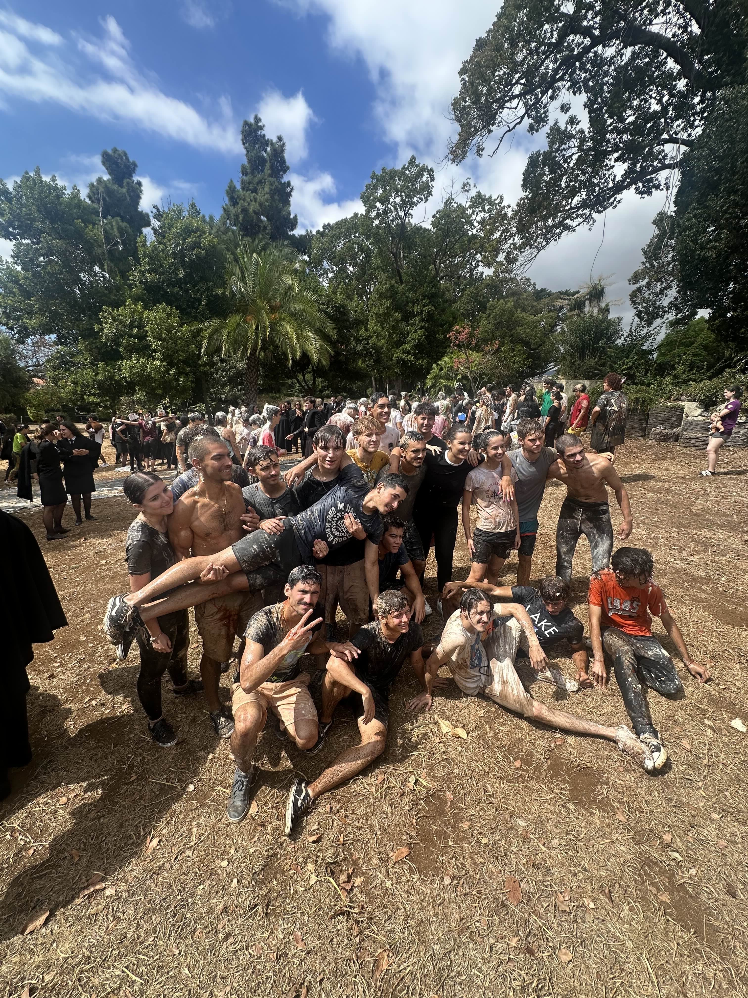 Estudantes posam juntos num jardim, segurando um colega na horizontal.