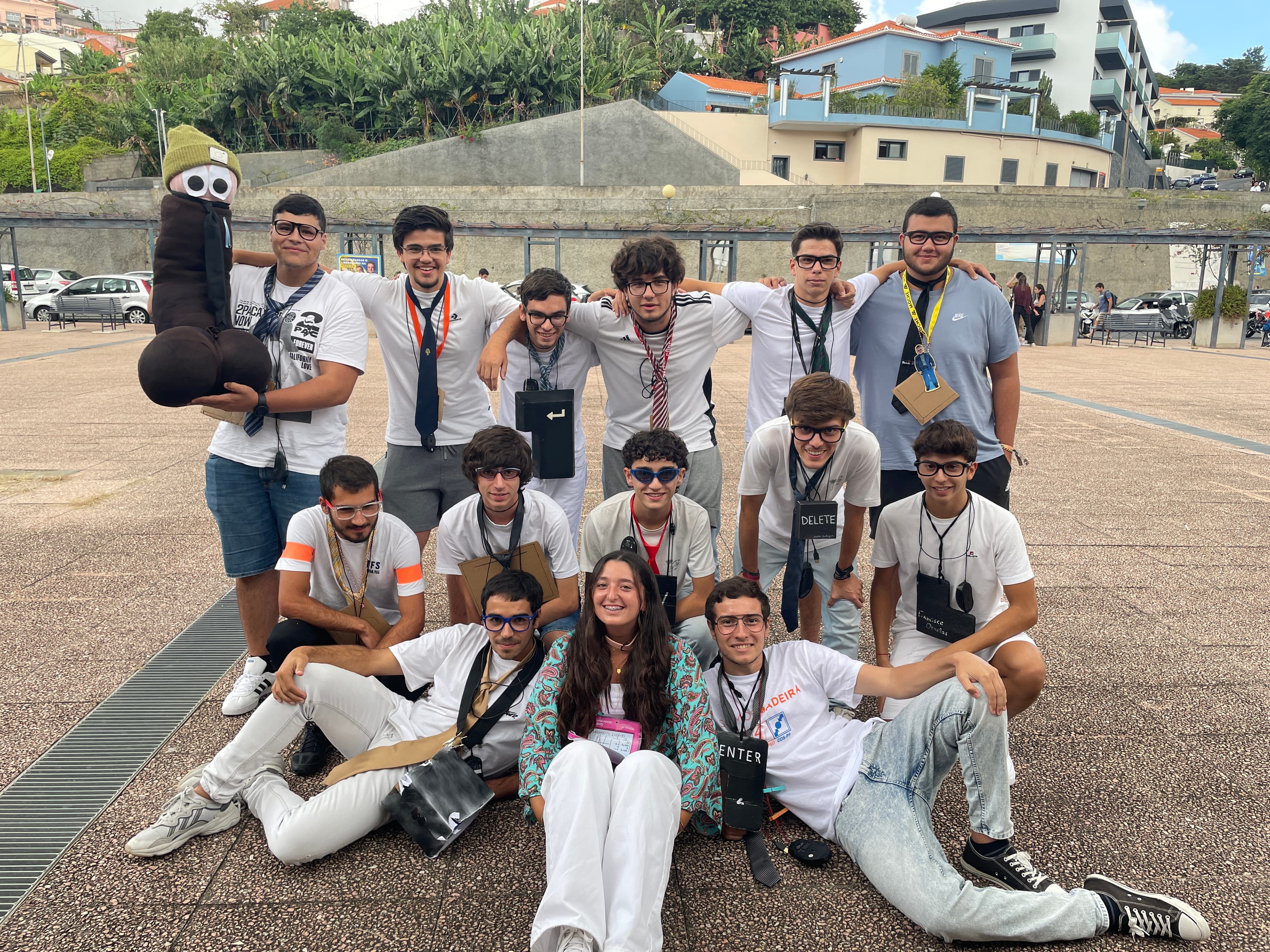 Grupo de estudantes com óculos, gravatas e placas de teclas de computador posa com a mascote.